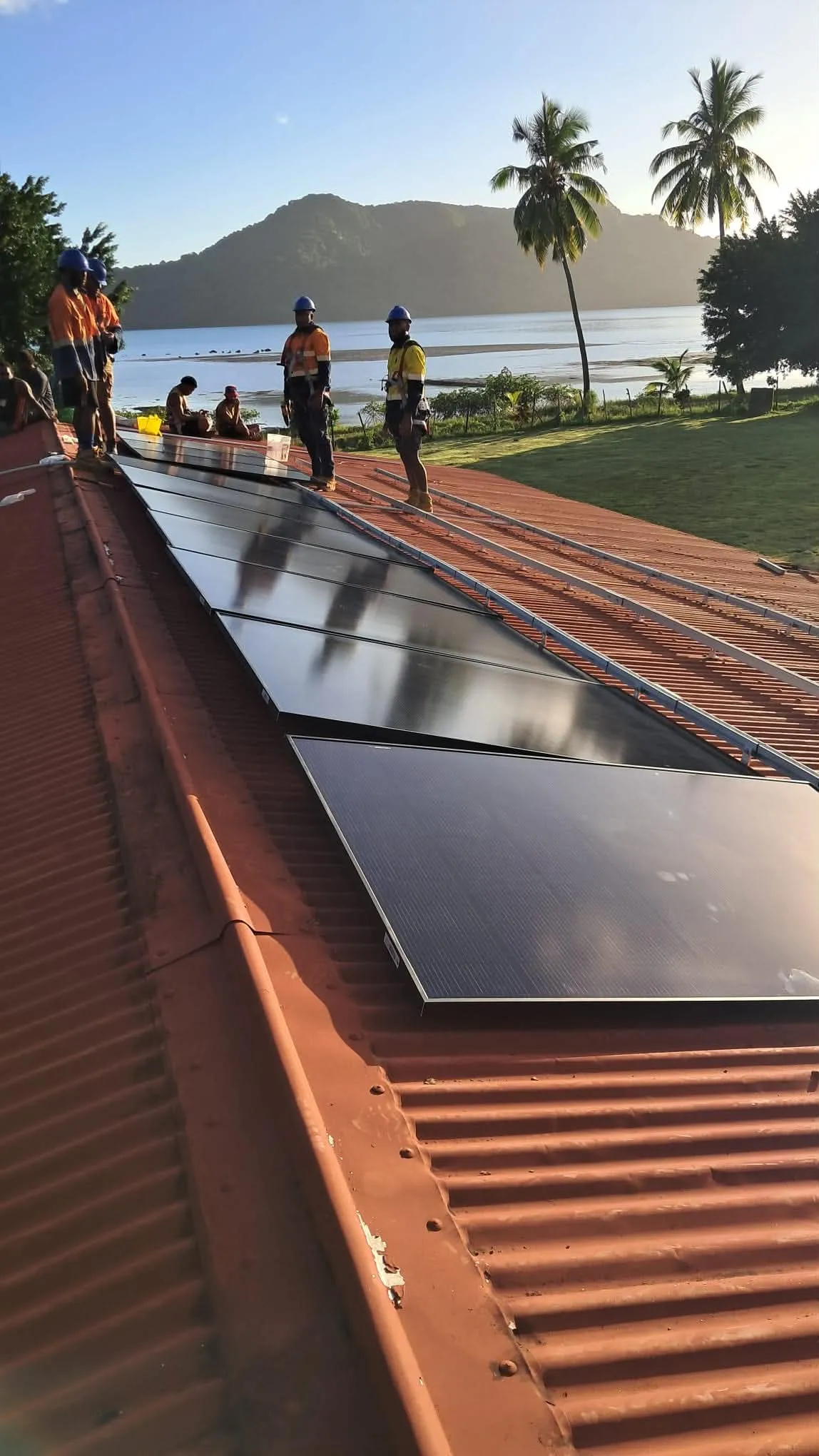 Pacific Sun Solar crew installing residential solar panels on a Fiji island roof at golden hour