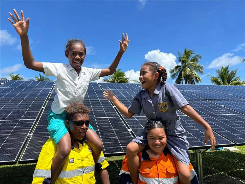 Fijian school children celebrating on installers' shoulders in front of a new solar array